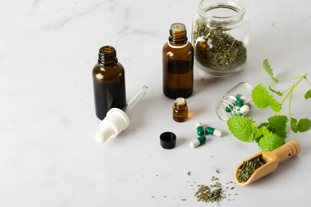 Homeopathic tinctures, capsules and dried herbs with fresh mint on a marble surface