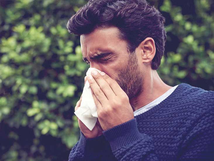 Man blowing his nose into a tissue outdoors during an allergy flare-up