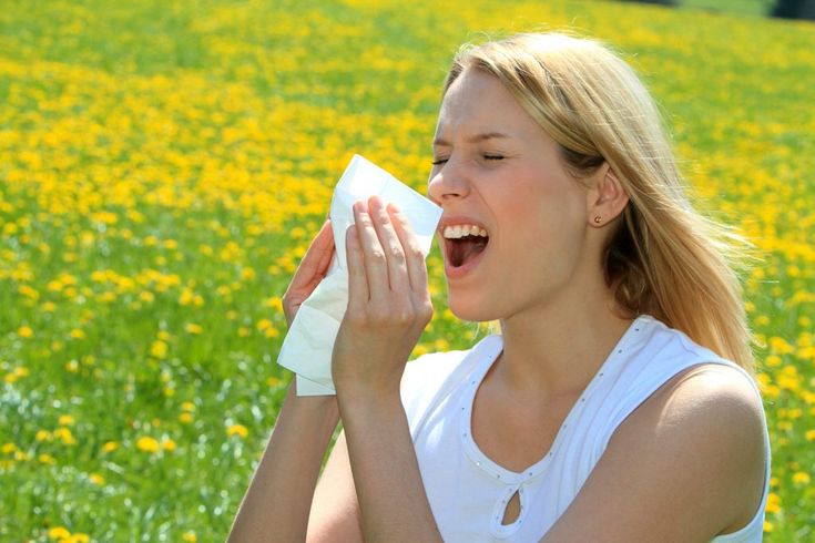 Woman sneezing into a tissue in a meadow of flowers in full bloom