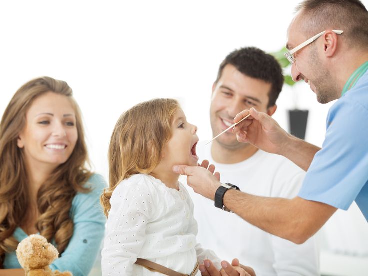 Doctor examining a young child’s throat while her parents look on