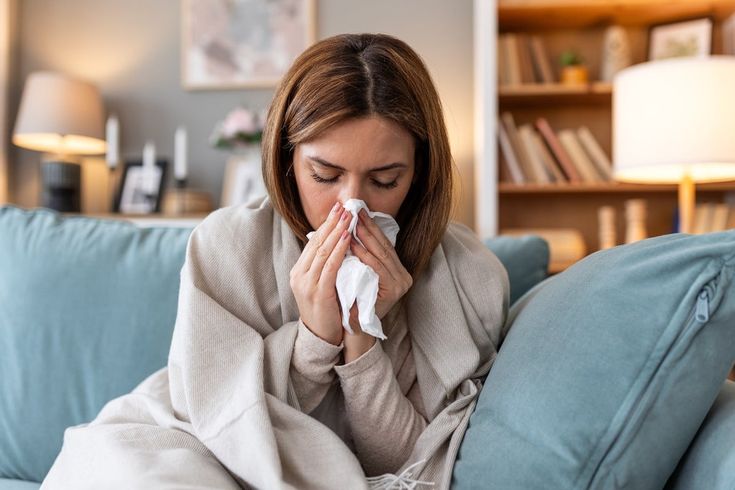 Woman blowing her nose while wrapped in a blanket at home