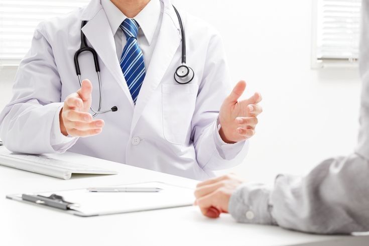 Homeopath talking a patient through their symptoms across a consulting-room desk